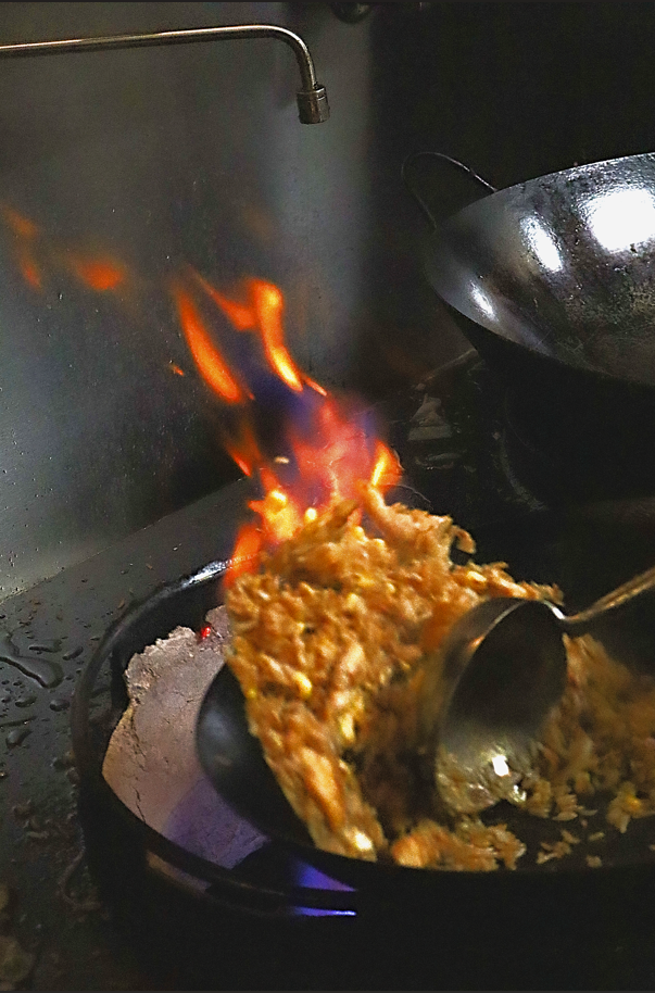 Fried rice cooking over a wok flame in Zimo's kitchen